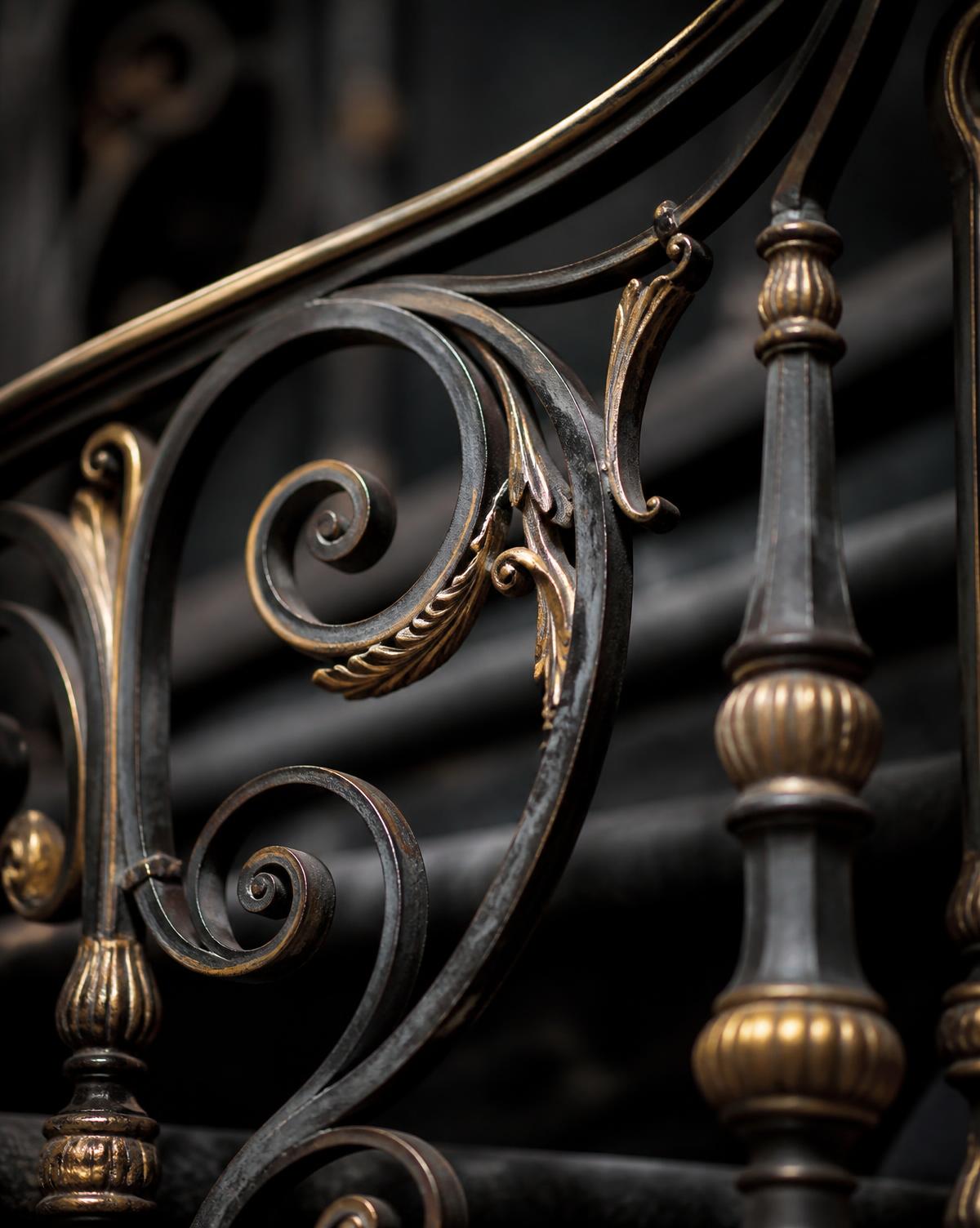 Détail d'escalier en fer forgé patiné, volutes et rehauts dorés